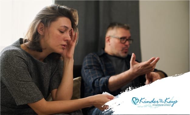 Woman looking distressed while a man gestures during a tense conversation, illustrating relationship conflict or emotional stress in a home setting.