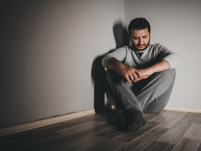 A depressed man sitting in the corner looking at the floor needing treatment