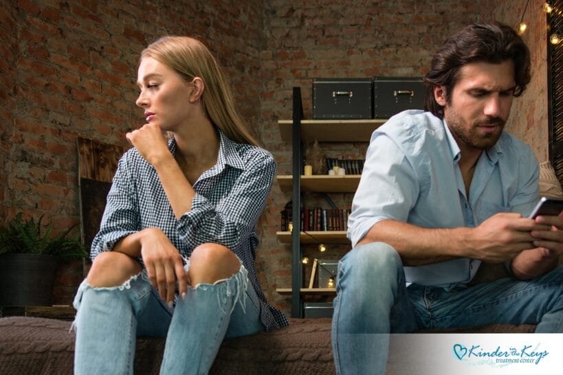 Woman appearing emotionally distant beside partner using a phone