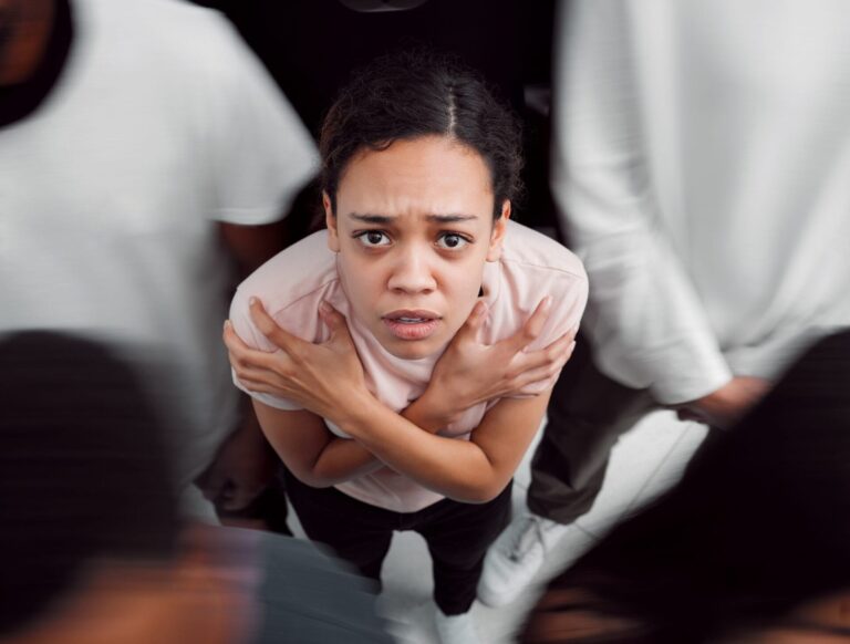 Woman looking upward with arms crossed over her chest while blurred people move around her