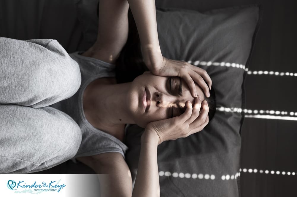 Woman lying on bed with hand on head, showing signs of PTSD and emotional distress.